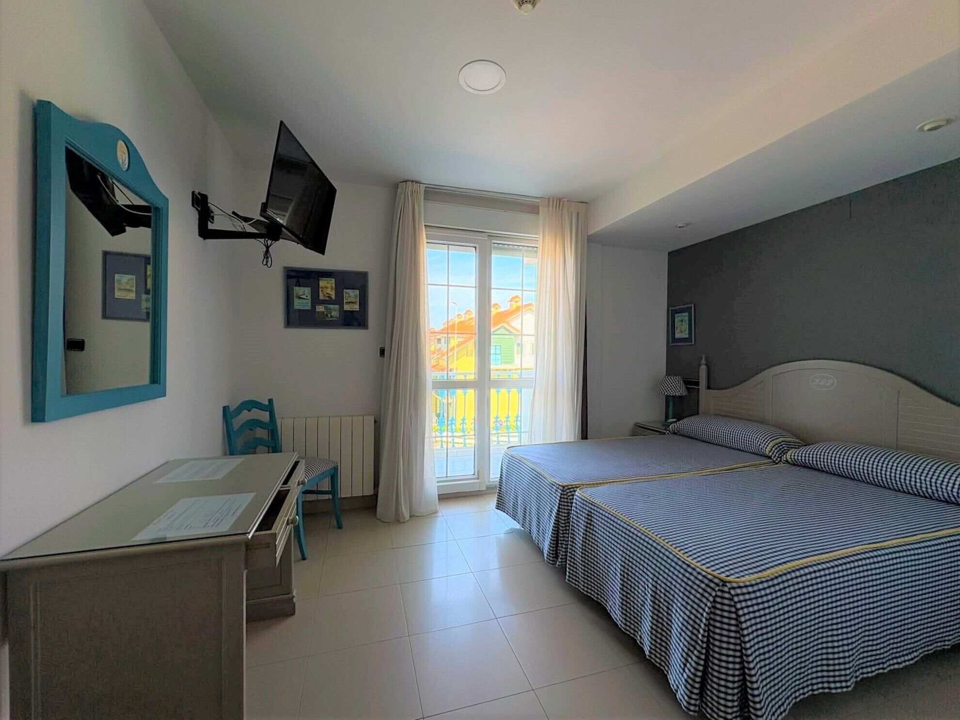 Un dormitorio con cama, escritorio, silla, televisor y ventana con cortinas.