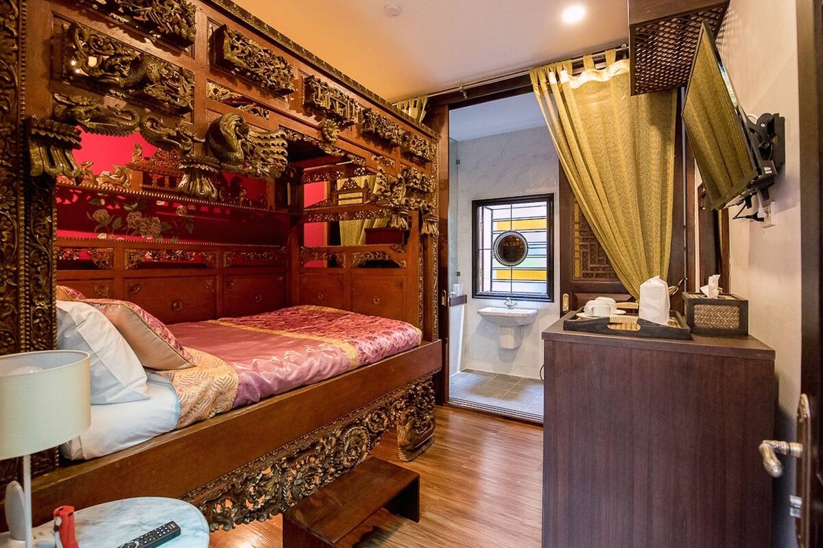 A traditional room with a wooden bed, ornate headboard, and a small bedside table with a lamp.