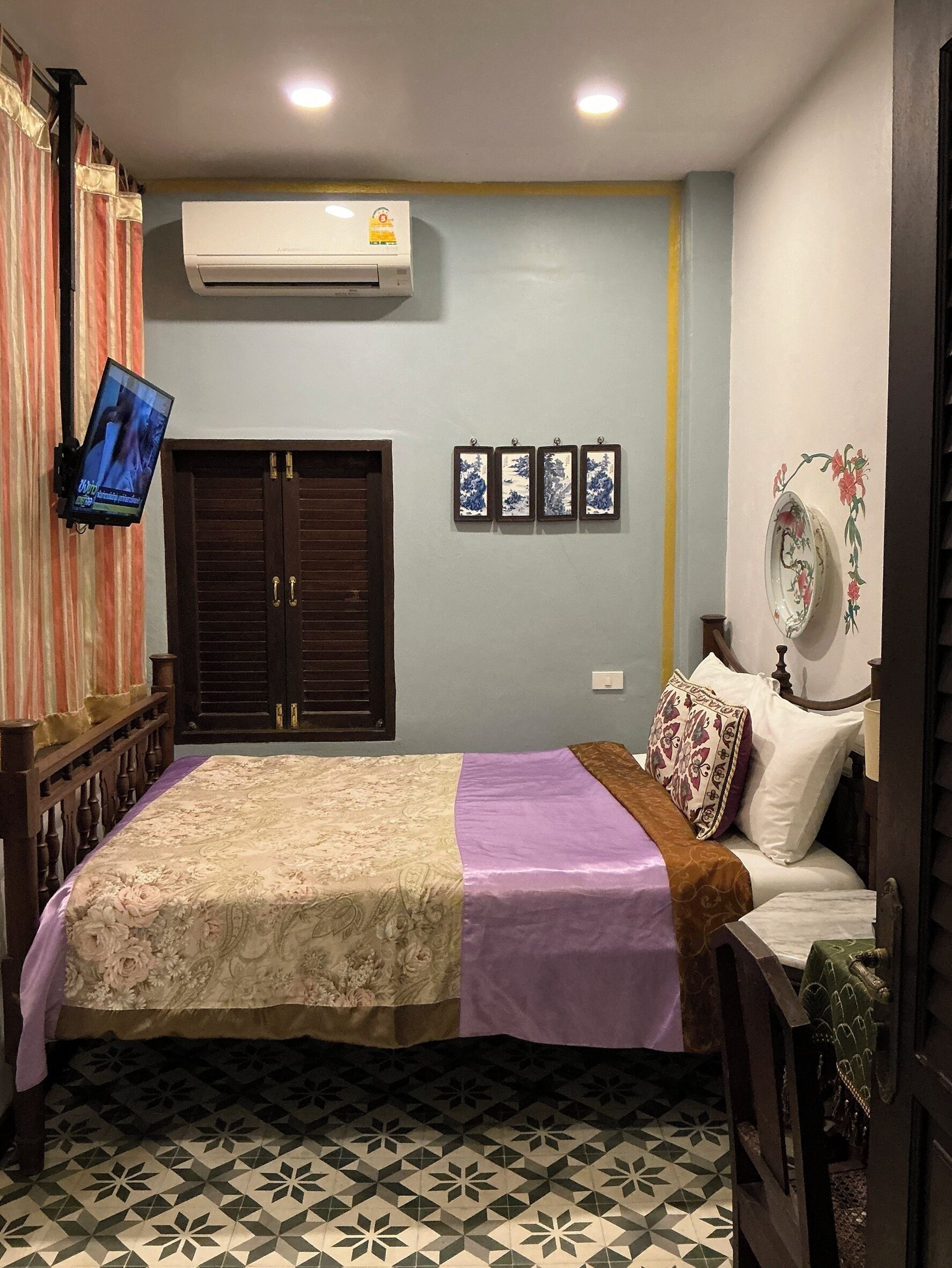 A bedroom with a bed, an air conditioner, a TV, a wardrobe, and a wall-mounted shelf with decorative items.