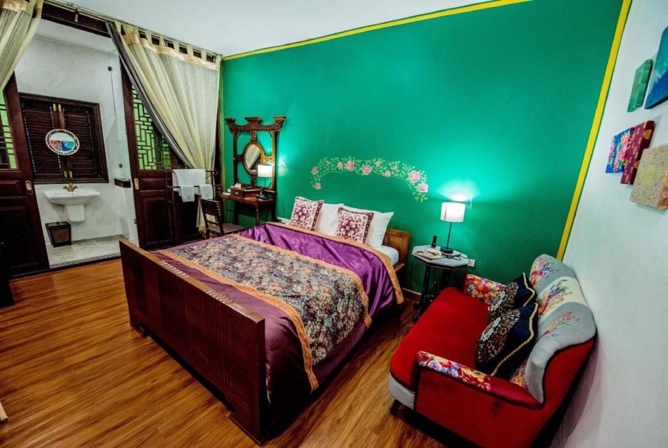 A bedroom with a wooden bed, a red chair, a small table, and a green accent wall.