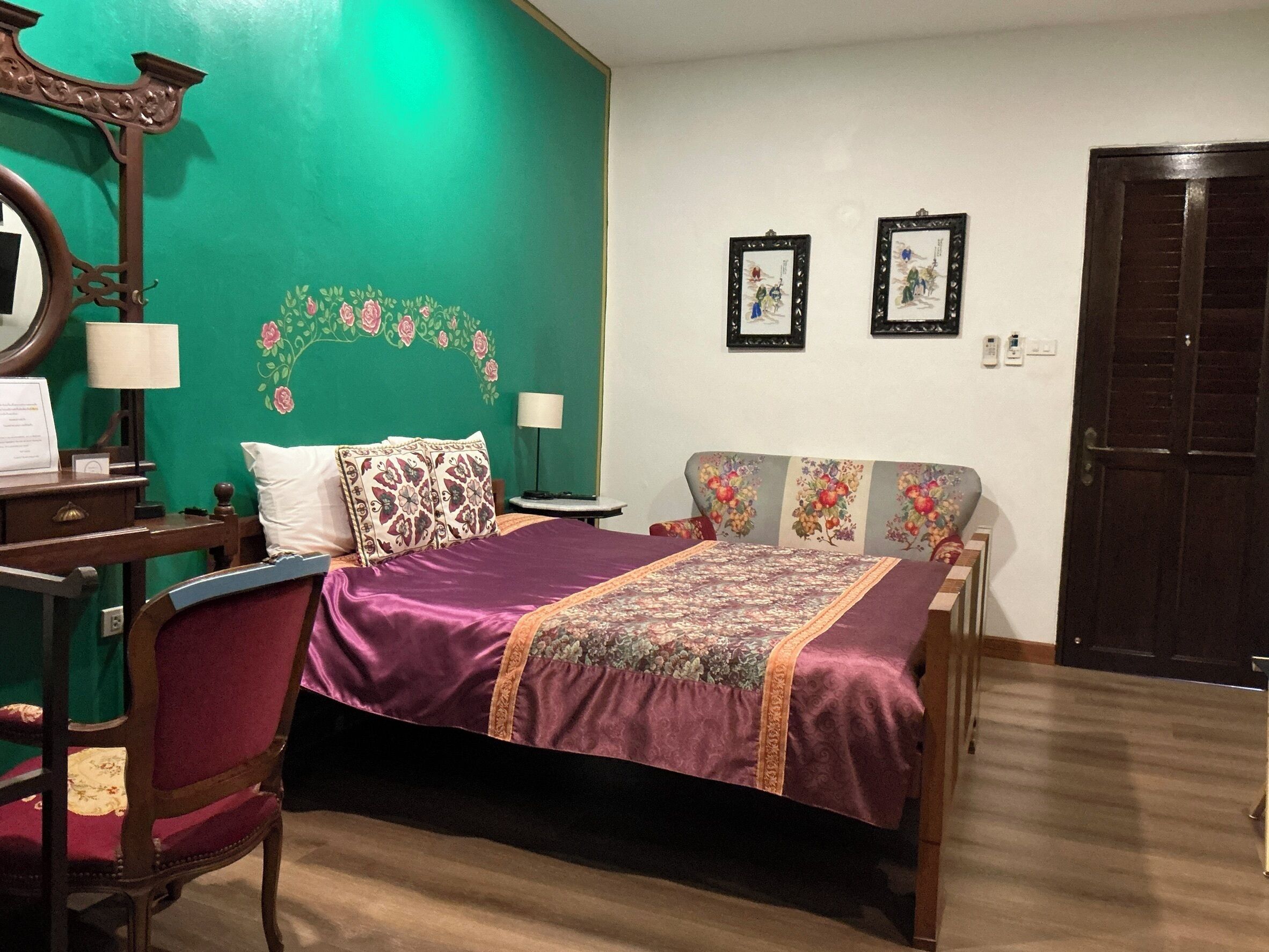 A room with a bed, a desk with a lamp, a chair, and two framed pictures on the wall.