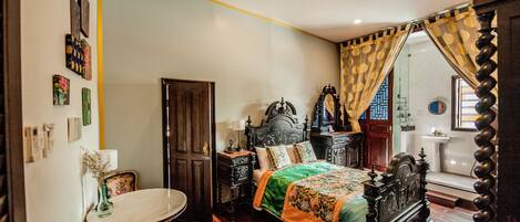 A traditional bedroom with a four-poster bed, a wooden wardrobe, a small round table, and a mirror.