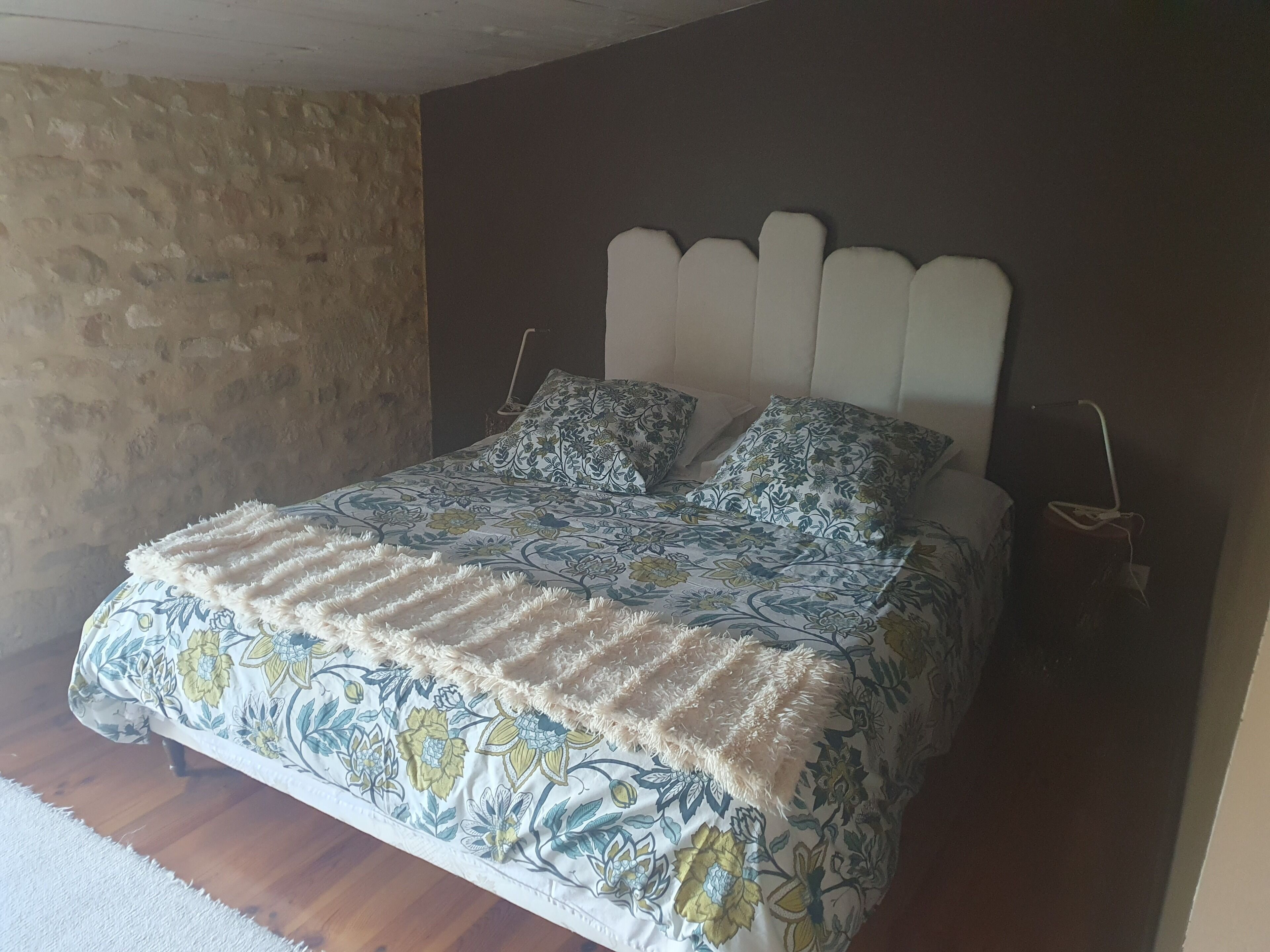 Una cama con colcha de estampado floral y dos almohadas a juego, un cabecero blanco y suelo de madera.