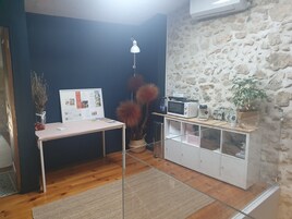 Cocina compacta con pared de piedra, una pequeña mesa con un tablón de anuncios, microondas, cafetera y planta en maceta.