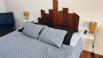 A neatly made bed with patterned bedding, a wooden headboard, a bedside table with a lamp, and a chair.