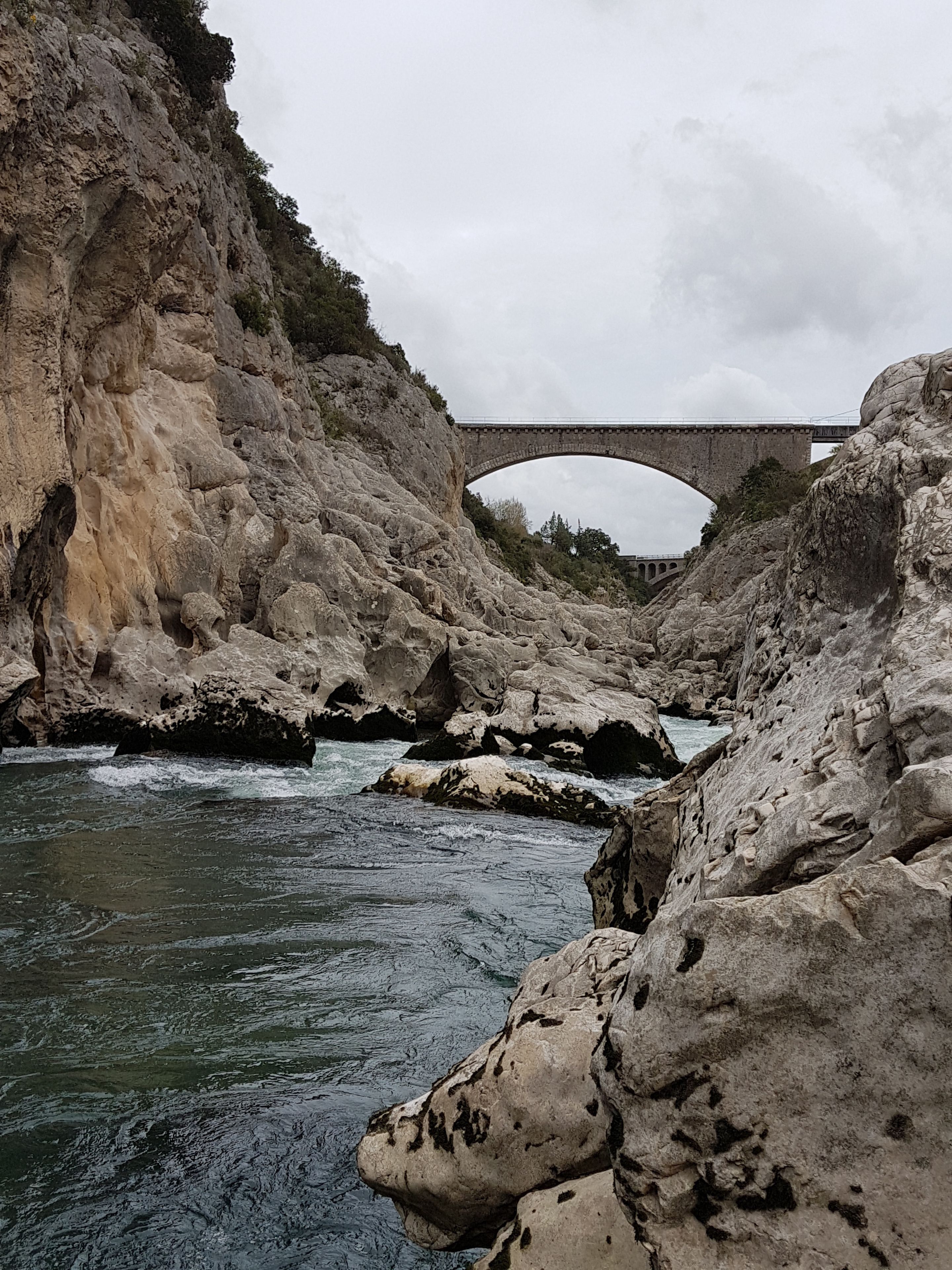 Un lecho de río pedregoso con un puente al fondo.