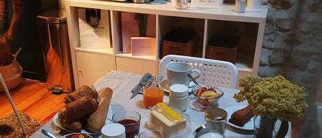 Una mesa de desayuno preparada con croissants, fruta, una cafetera y un florero con flores.