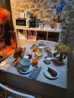 Una mesa de desayuno preparada con croissants, fruta, una cafetera y un florero con flores.