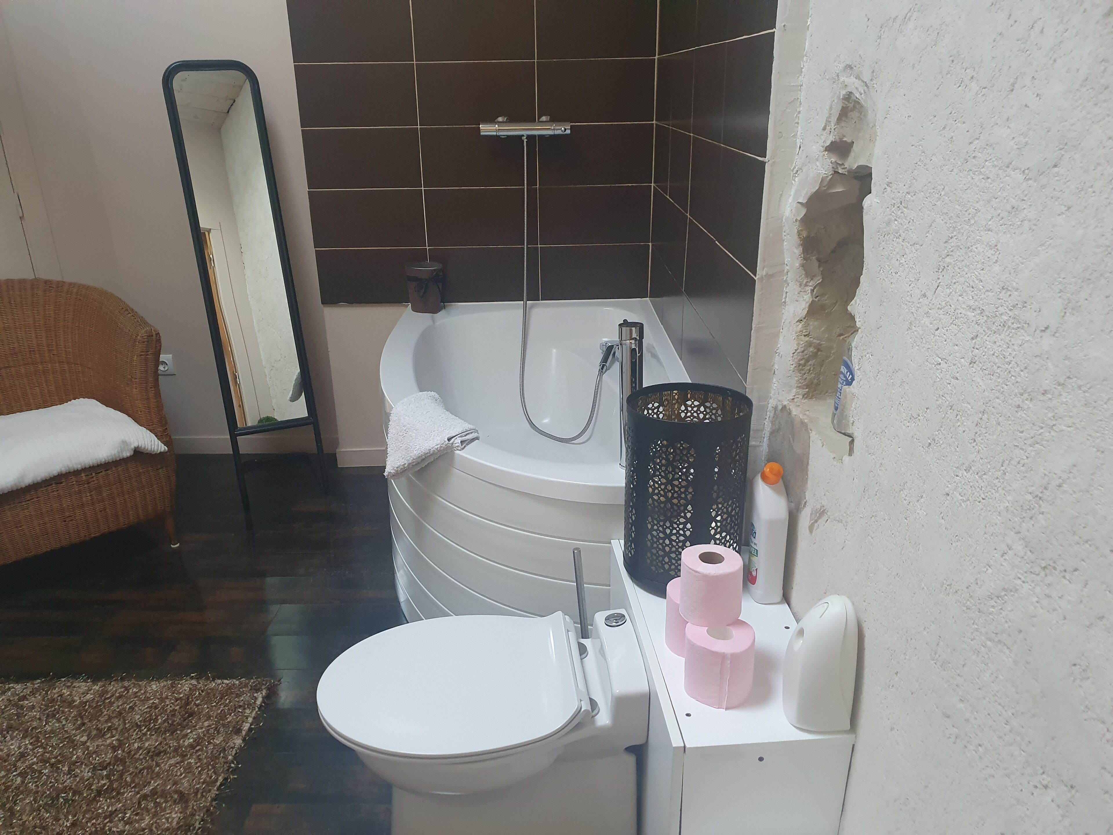A bathroom with a white bathtub, a toilet, a wicker chair, and a mirror.
