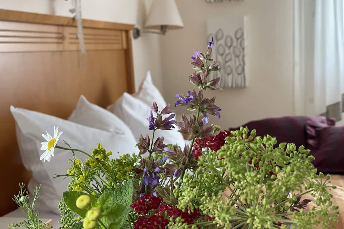 Een hotelkamer met een bed, kussens, een nachtkastje en een bloemenarrangement.