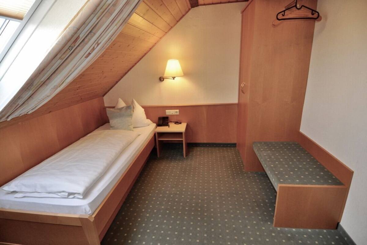 Een knus, klein kamertje met een enkel bed, een bureau en een bankje.
