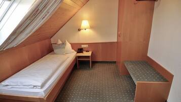 A small, cozy room with a single bed, a desk, and a bench.