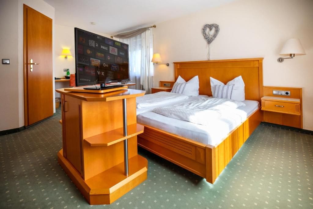 A hotel room with a bed, a desk, a television, and a heart-shaped wall decoration.