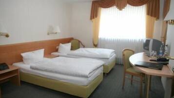 A hotel room with two single beds, a desk with a chair, a television, and a window with curtains.