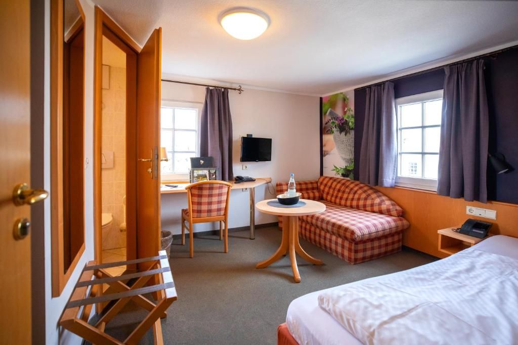 A hotel room with a bed, a sofa, a desk with a chair, a television, and a window with curtains.