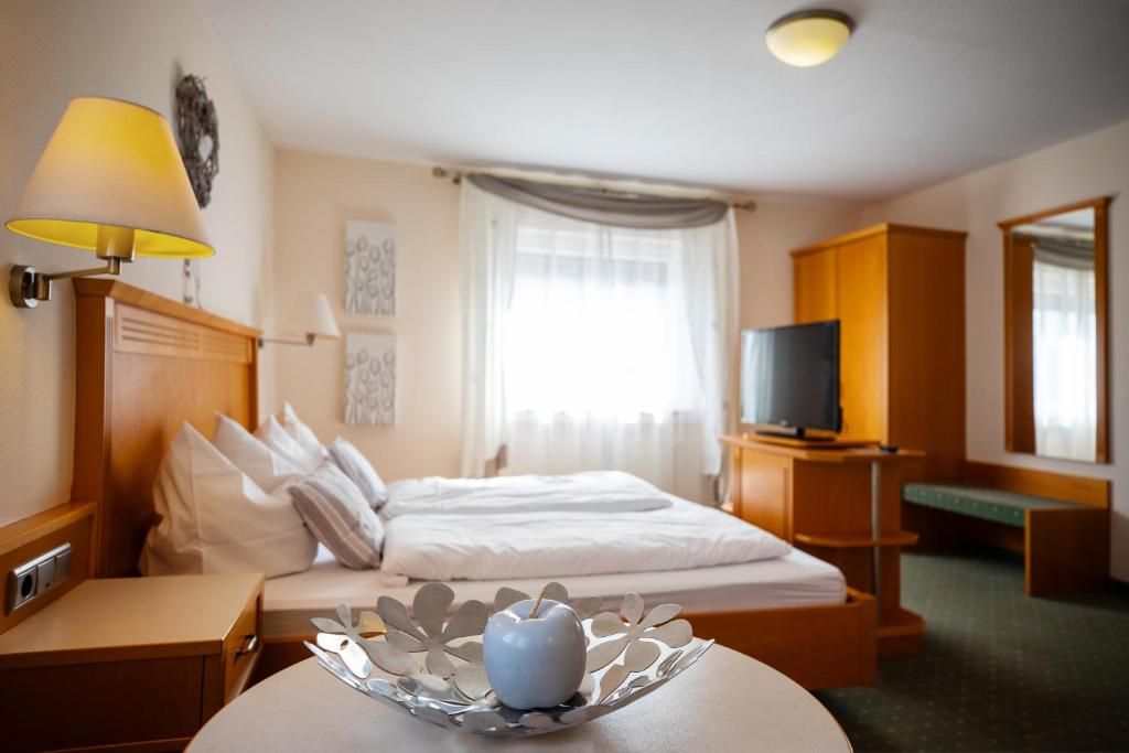 A hotel room with a bed, bedside table, lamp, television, and a decorative bowl on the table.