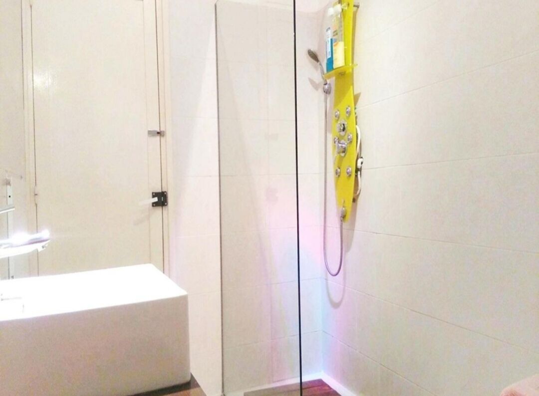 Un baño con una bañera blanca, cabina de ducha de vidrio y un cabezal de ducha manual amarillo.