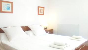 Una cama bien hecha con sábanas y almohadas blancas, una mesita de noche con lámpara, y dos cuadros en la pared.
