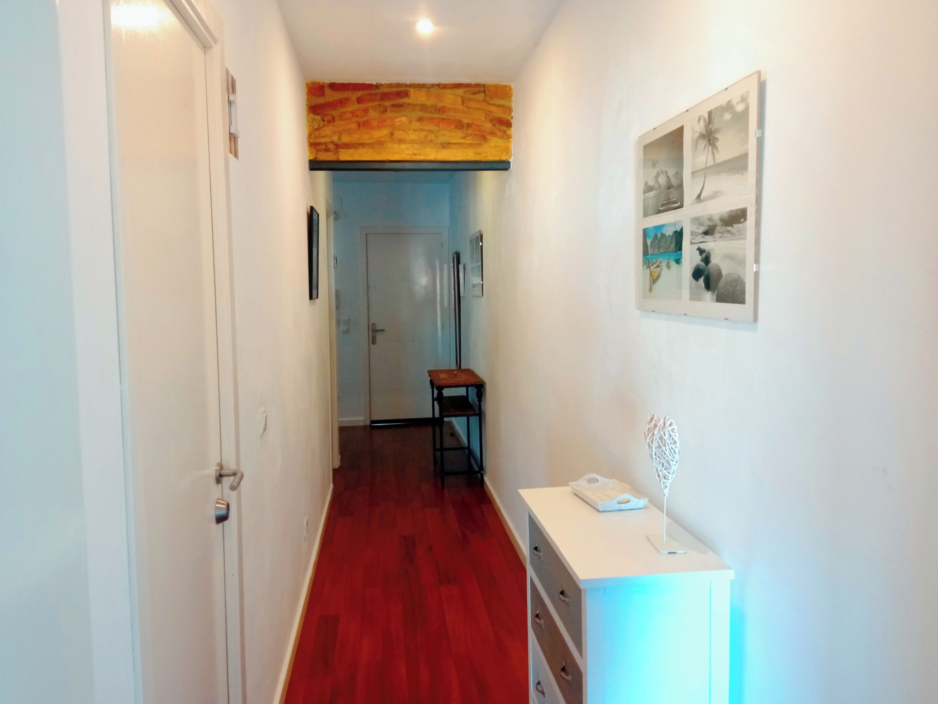A hallway with a red wooden floor, a white door on the left, and a white cabinet with drawers on the right.