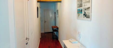 A hallway with a red wooden floor, a white door on the left, and a white cabinet with drawers on the right.