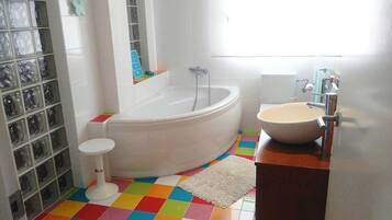 Un baño con una bañera blanca, un lavamanos redondo y un piso colorido.