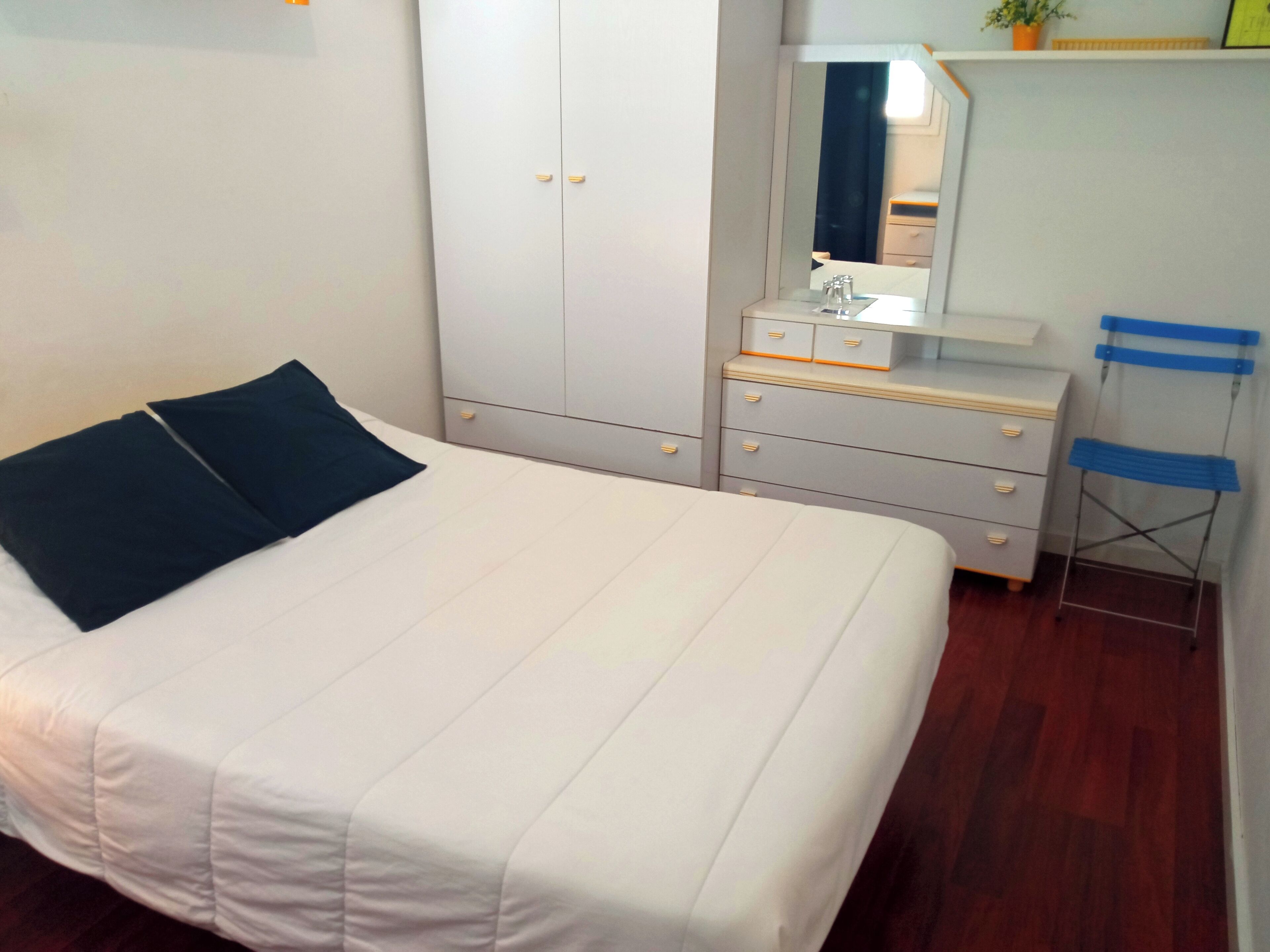 A bedroom with a bed, a wardrobe, a dresser, a mirror, and a chair.