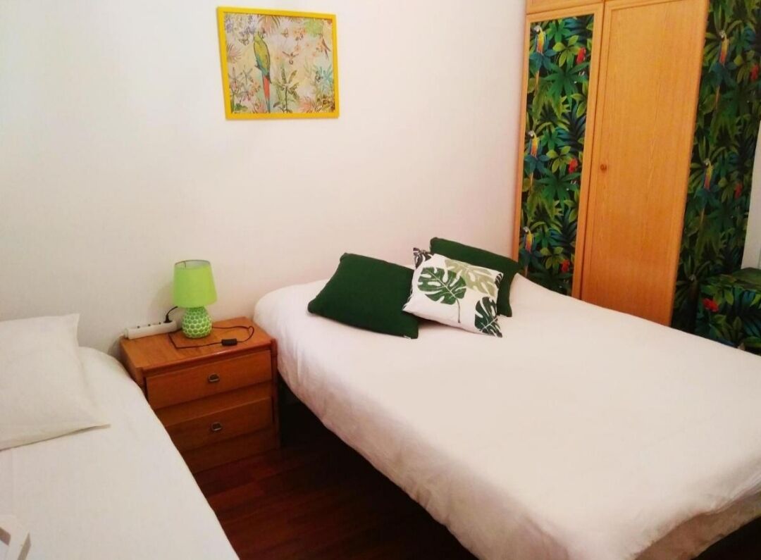 Un dormitorio con una cama individual, una mesita de noche con lámpara, un armario de madera y una pared decorada con un cuadro floral.