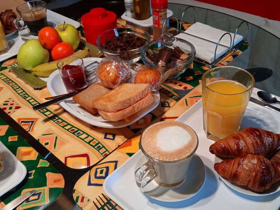 Una mesa de desayuno con diversos alimentos y bebidas, como croissants, tostadas, fruta y una taza de café.