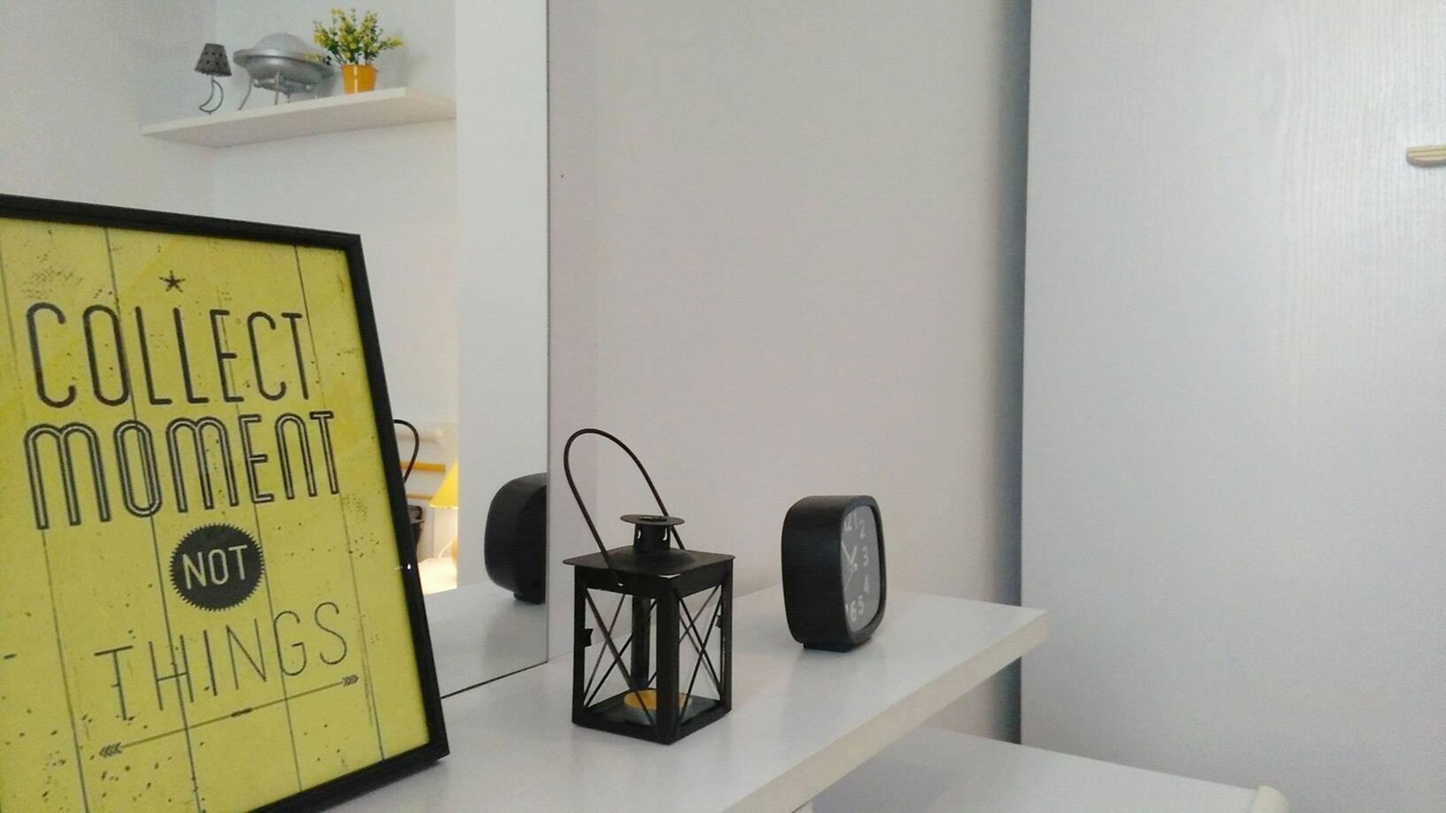 Una frase motivacional en un marco sobre una pared, un farol negro y dos altavoces sobre un estante blanco.