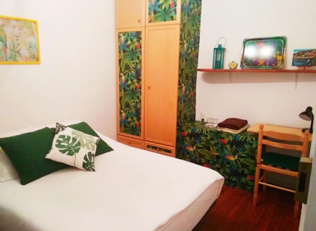 Una camera da letto con un letto, un'armadiatura in legno, una scrivania con una sedia e uno scaffale con vari oggetti.