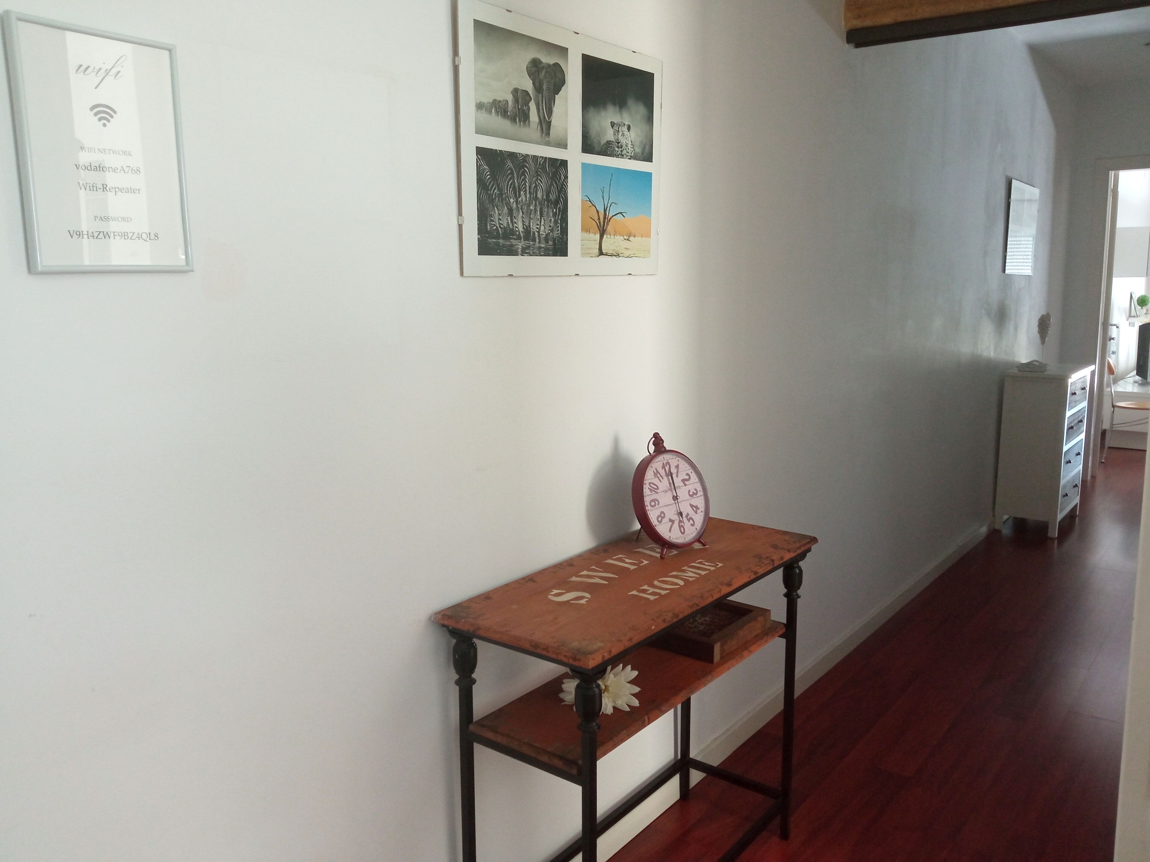 Un pasillo con un cartel de contraseña de WiFi enmarcado, un reloj y fotografías de fauna enmarcadas en la pared.