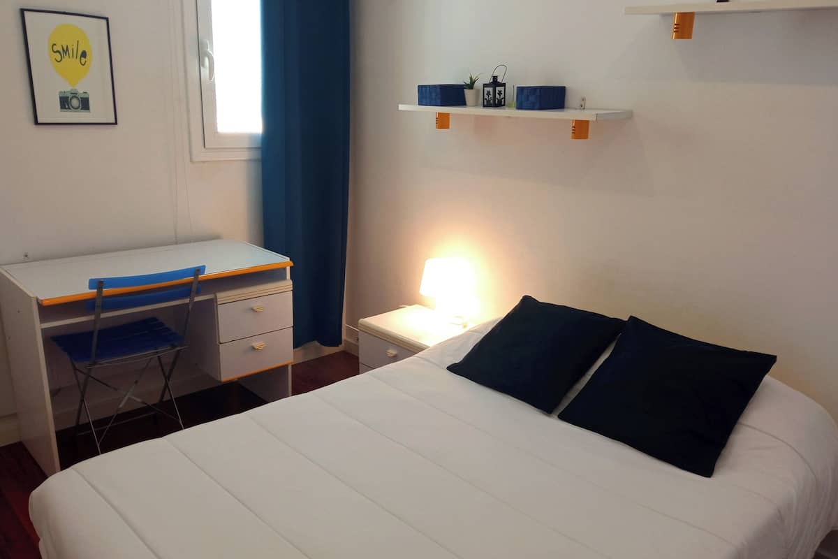 Ein Schlafzimmer mit Bett, Schreibtisch, Stuhl, Nachttisch und einer Wandablage mit Dekoration.