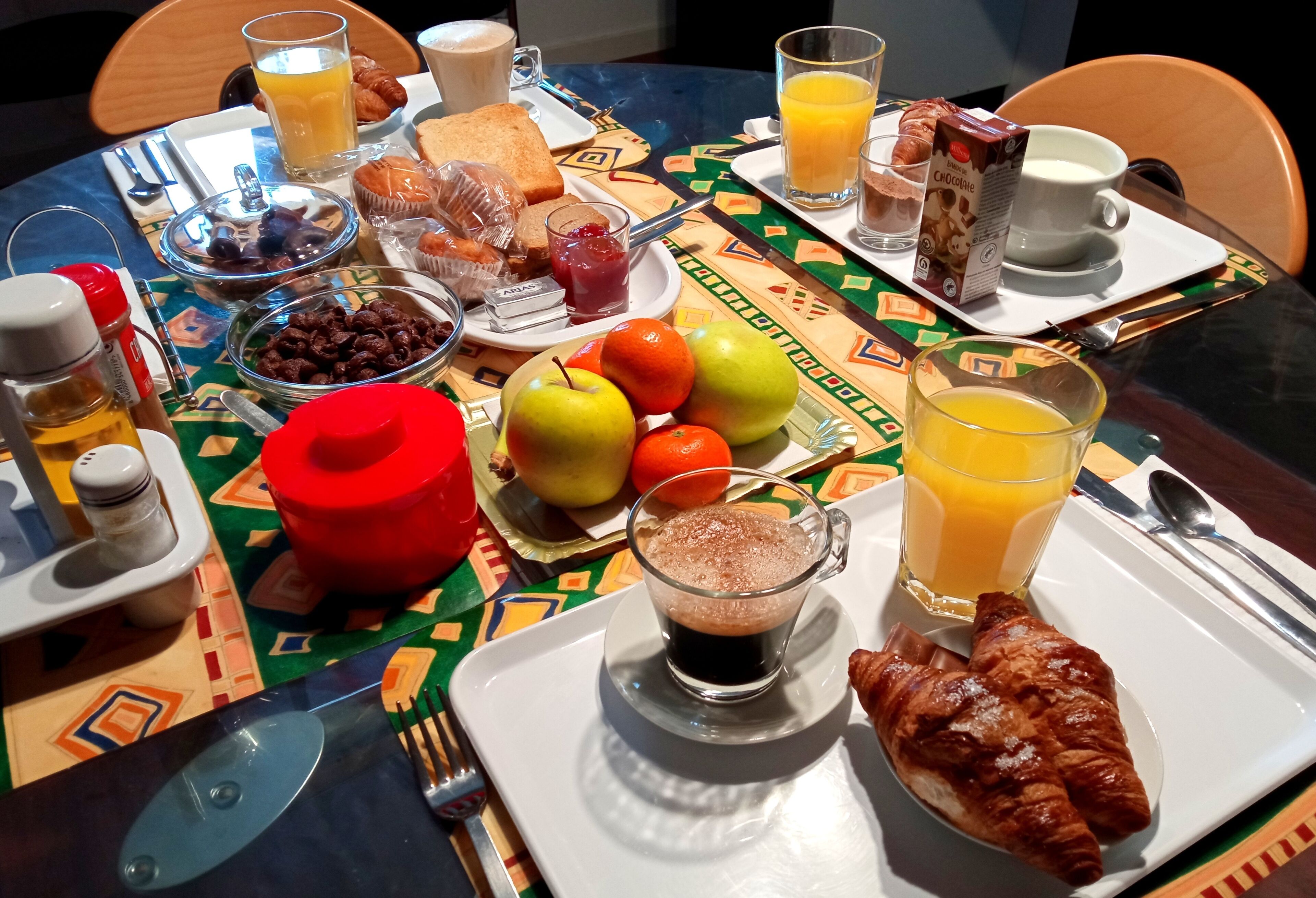 A breakfast table with various food items, including toast, eggs, fruits, and beverages.