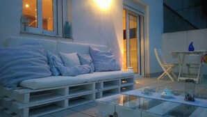 A modern outdoor seating area with a white sofa, cushions, and a glass coffee table. - Habitacions Sant Pere Claver (Tarrega)