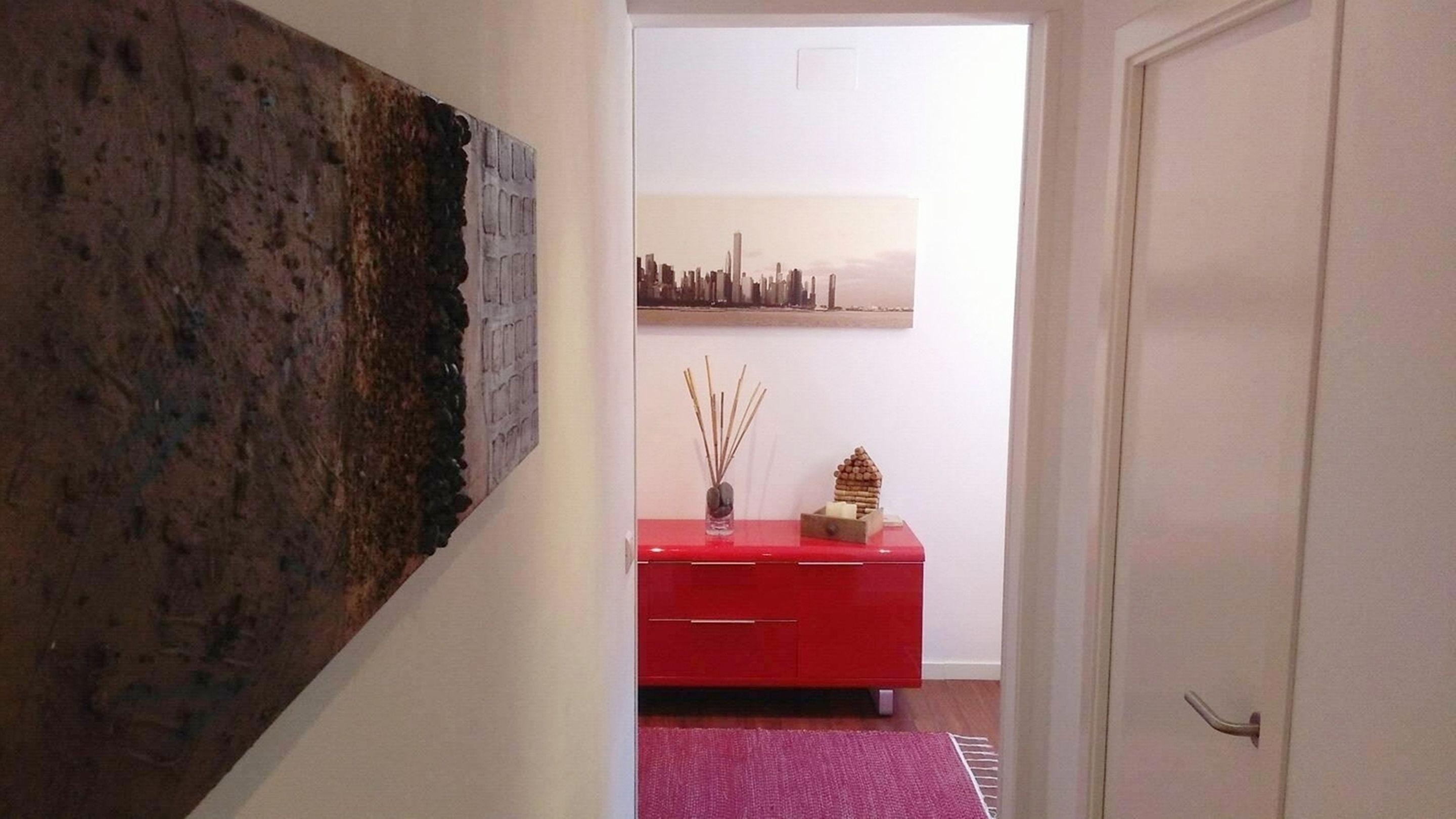 Een gang met een rode kast, een stadslandschap schilderij en een structuurwand.
