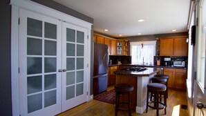 A kitchen with a central island, wooden cabinets, a refrigerator, and a window with blinds. - Comfort and Grace on Queen Anne Hill (Seattle)