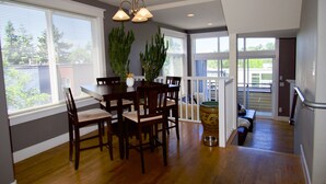 A dining area with a wooden table and chairs, a potted plant, and a view of the outdoors through large windows. - Comfort and Grace on Queen Anne Hill (Seattle)