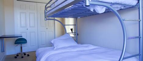A bunk bed with a desk and chair in a room with a door and carpeted floor.
