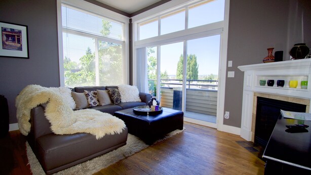 A living room with a brown leather sofa, a fluffy white throw blanket, and a black ottoman with a tray. There is a fireplace with colorful vases on the mantel. - Comfort and Grace on Queen Anne Hill (Seattle)