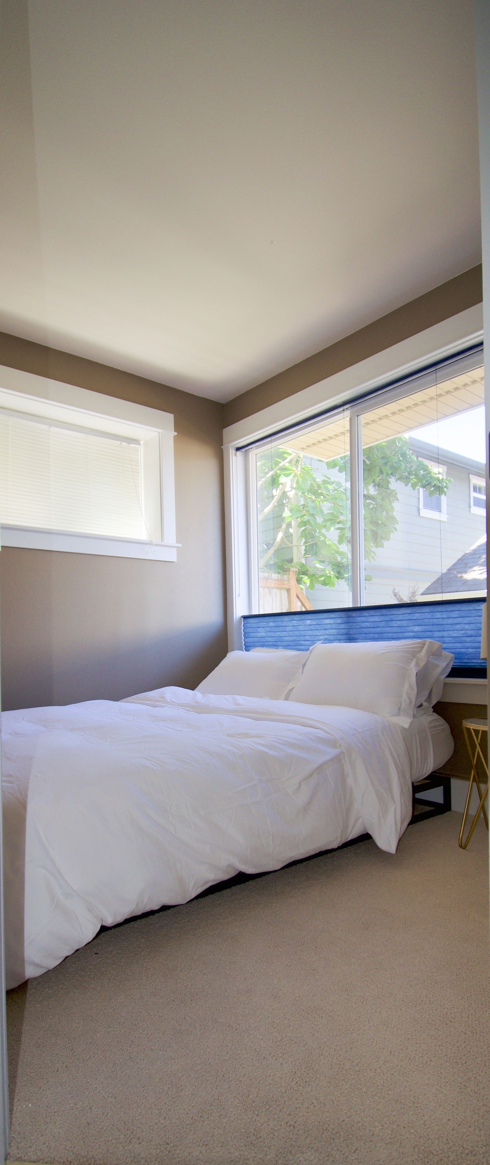 A bedroom with a single bed, a window with blinds, and a view of a tree outside.