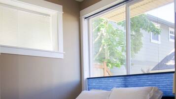 A bedroom with a single bed, a window with blinds, and a view of a tree outside.