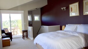 A bedroom with a large bed, a chair, a small table, and a view of the outdoors. - Comfort and Grace on Queen Anne Hill (Seattle)