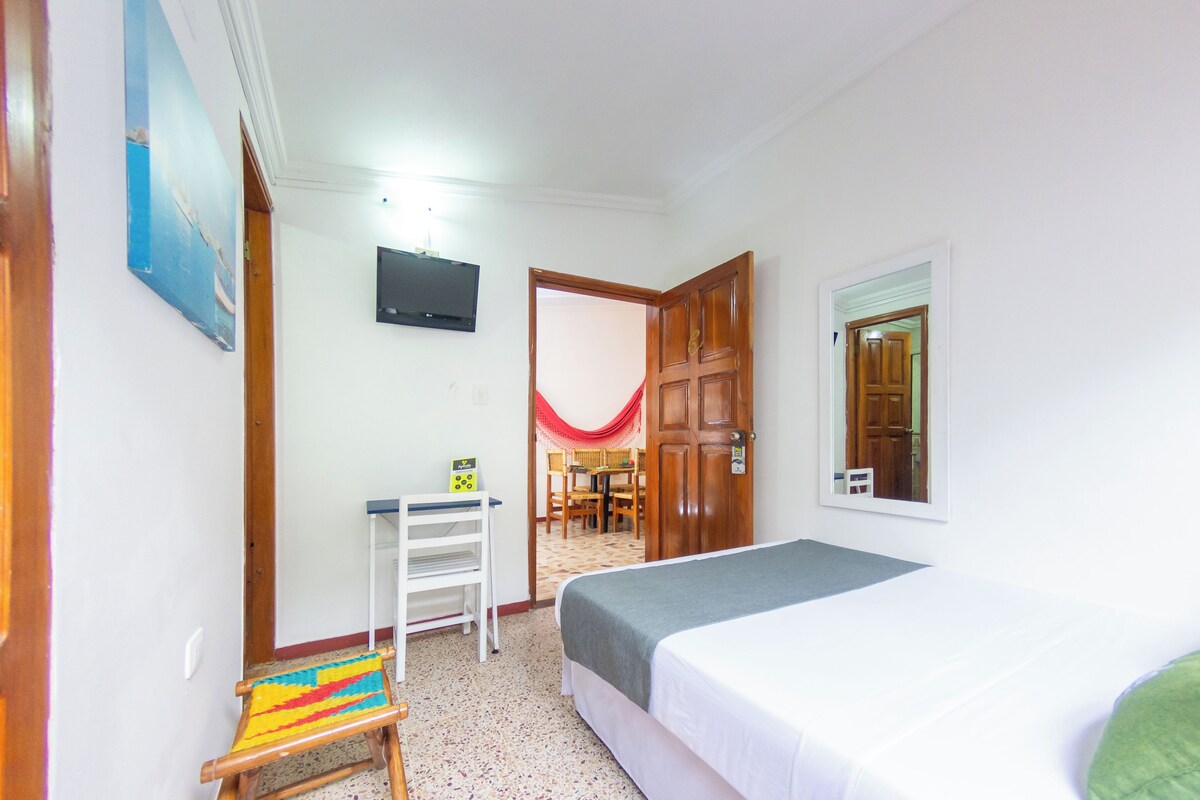 Una habitación con cama, escritorio, silla y televisor en la pared.