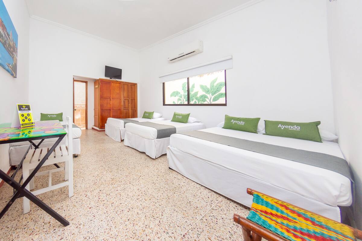 Habitación de hotel con cama, una mesita y una silla. Se ve vegetación por la ventana.