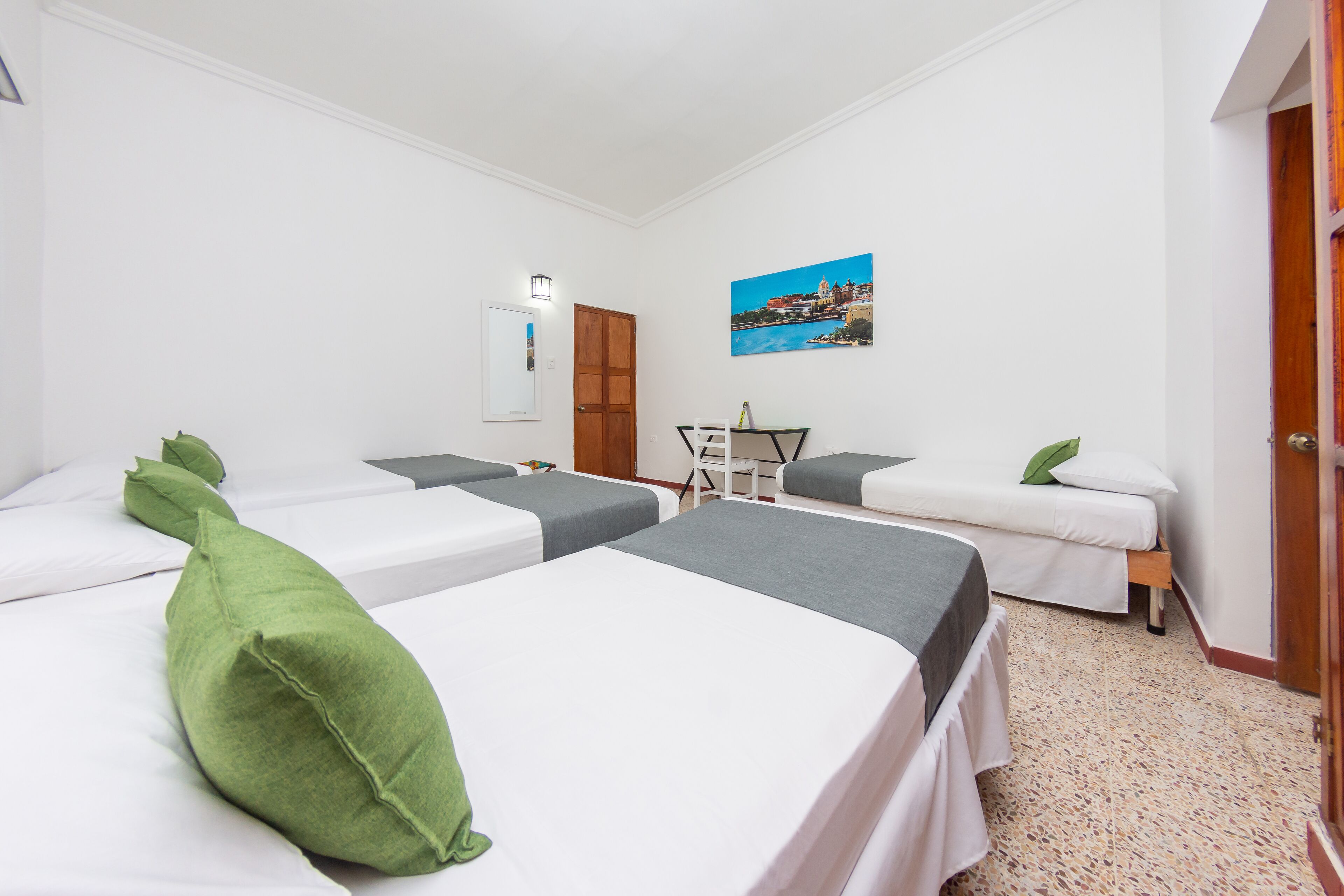 Habitación de hotel con dos camas individuales, un escritorio, una silla y un cuadro en la pared.
