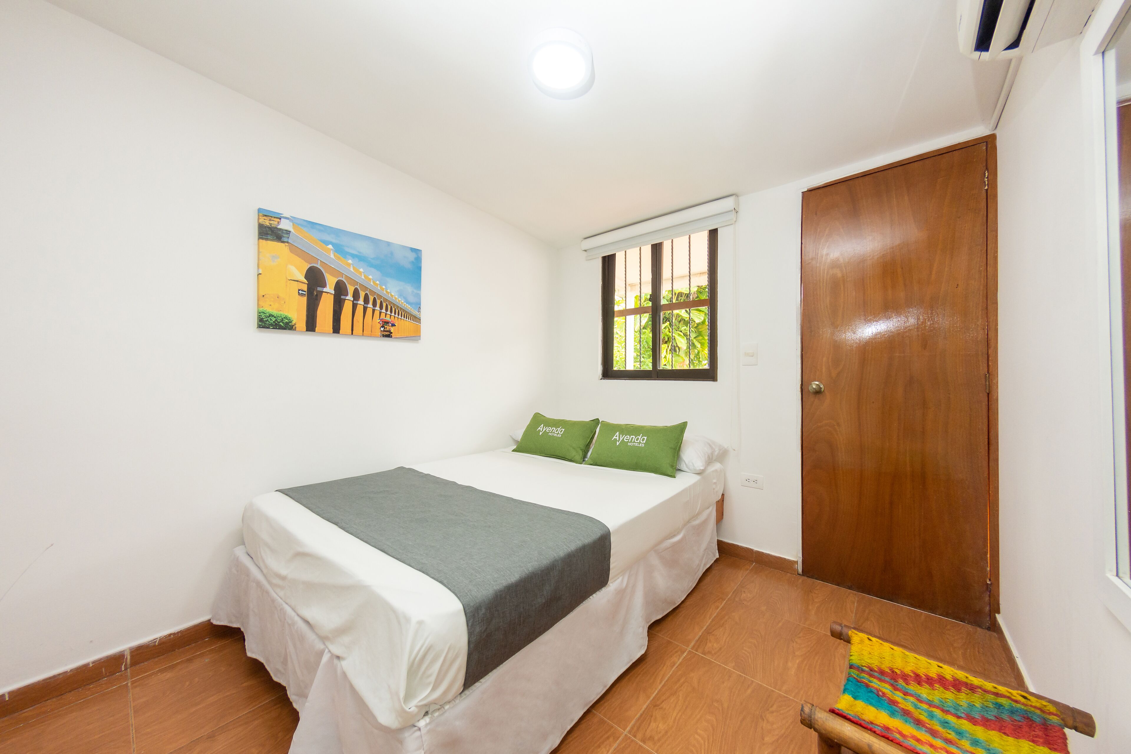 Een slaapkamer met een bed, een schilderij, een raam en een deur.