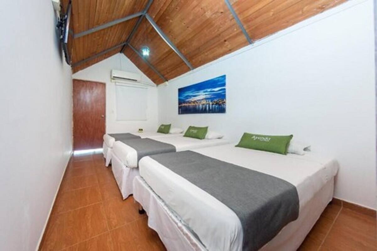 Una habitación con dos camas, techo de madera, un cuadro de un paisaje urbano y una puerta.