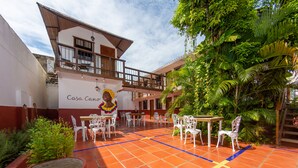 Un patio con mesas al aire libre, un edificio con un mural y abundante vegetación.