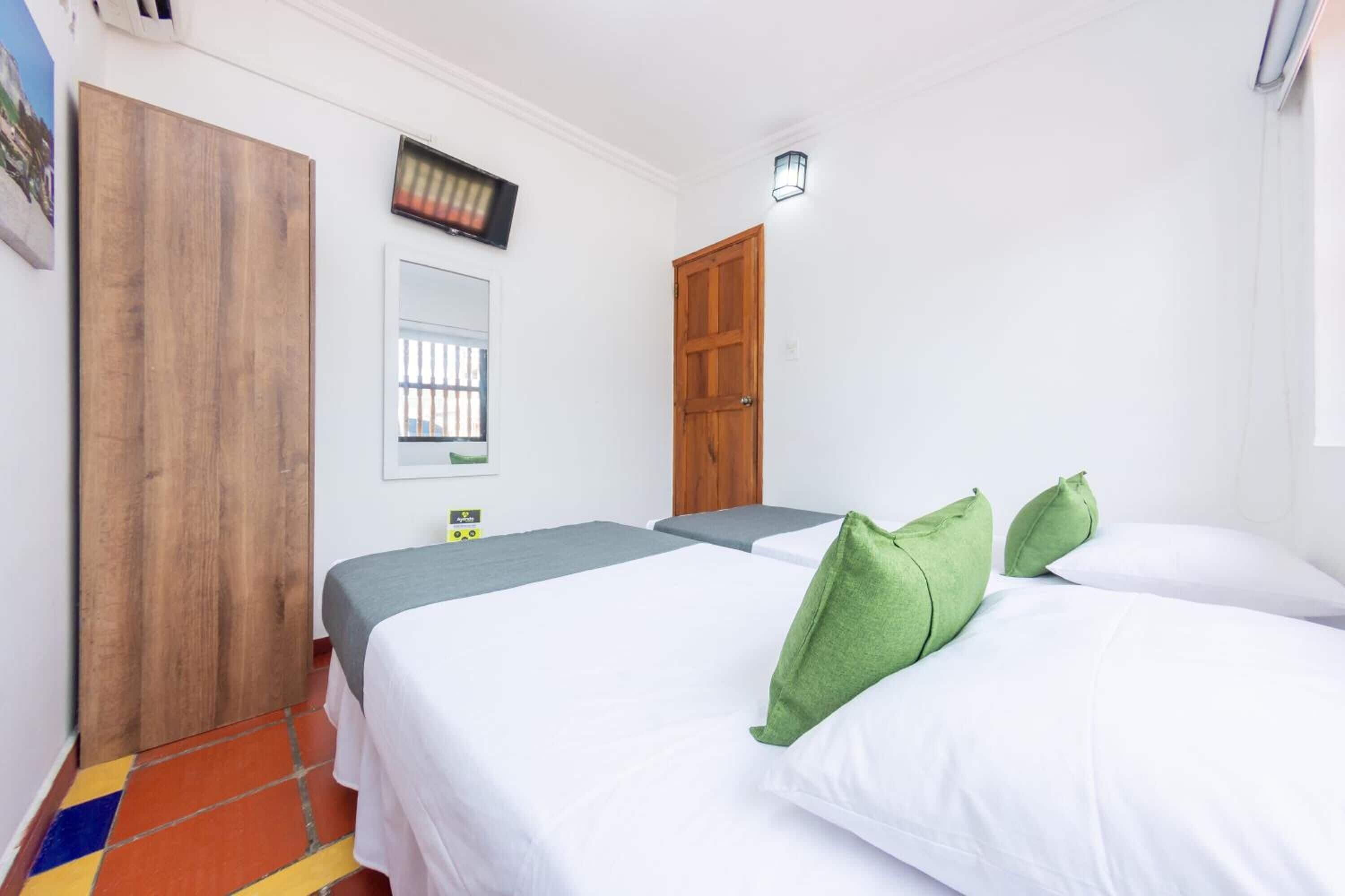 Habitación de hotel con dos camas, un armario de madera, un espejo y un televisor en la pared.