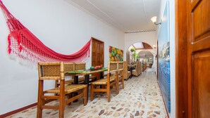 Un pasillo con sillas y mesas de madera, un paño rojo colgante y suelo de baldosas.